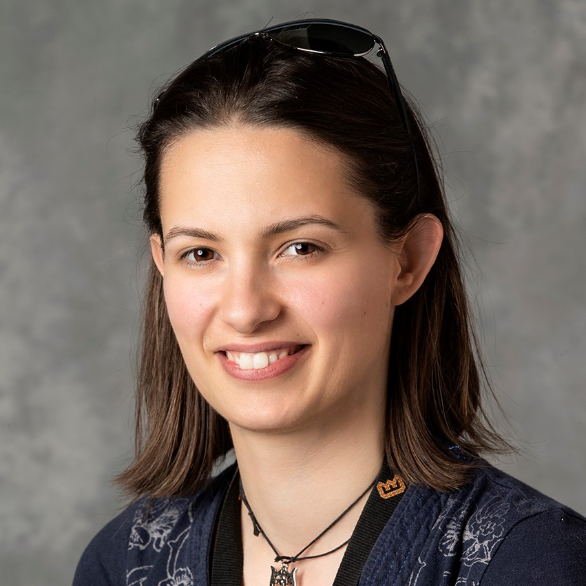 A picture of Giulia, a white woman with shoulder length brown hair wearing a pair of glasses on her head and smiling
